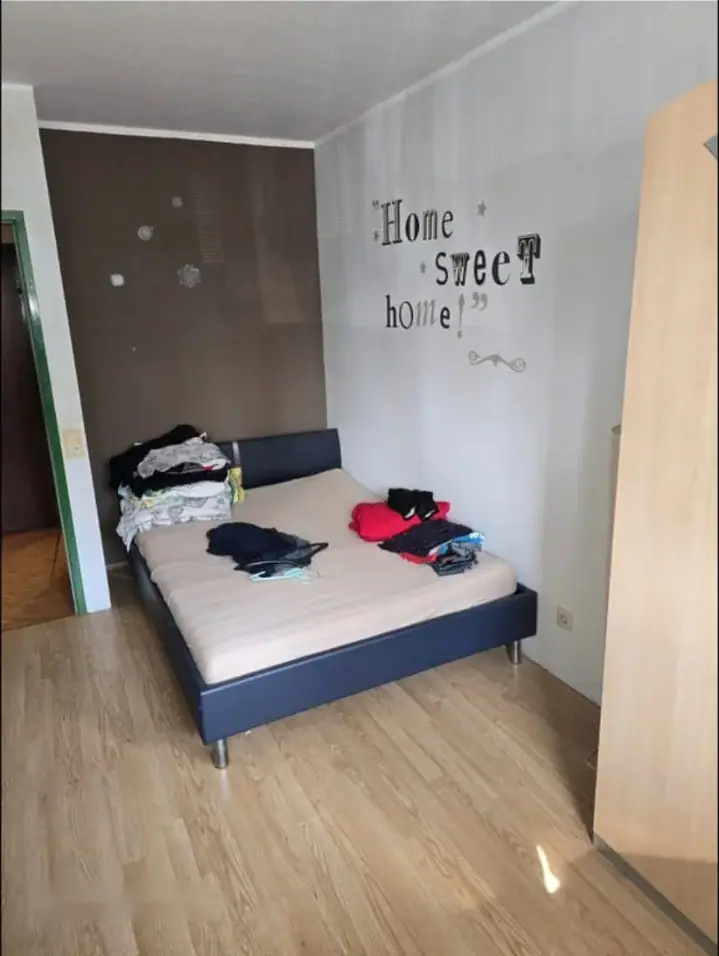 Schlafzimmer mit Bett, Kleidung und offenem Kleiderschrank